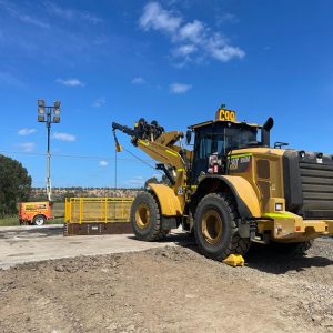 Wheel loader at a construction site with equipment and vehicles in the background.